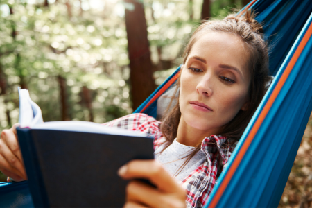 Tiener leest een boek terwijl ze in een hangmat ligt.