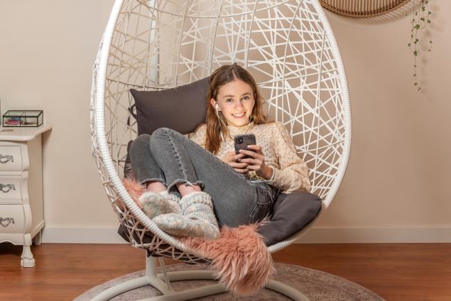 Evy (12) zit met opgetrokken knieën en mobieltje in haar hangstoel