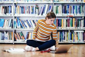 student met chromebook zit in kleermakerszit in een bibliotheek