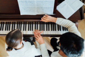 Pianodocent helpt een leerling bij de juiste vingerzetting op de piano